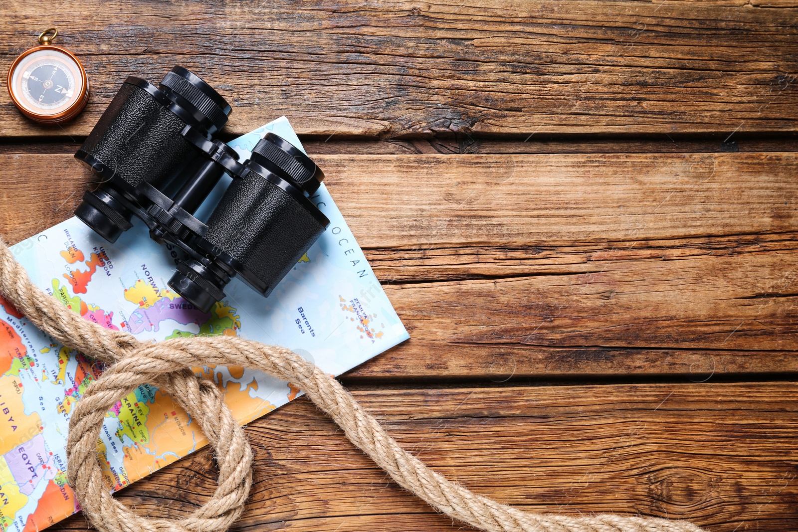 Photo of Binoculars, compass, world map and rope on wooden table, flat lay. Space for text