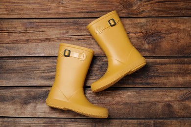 Photo of Pair of yellow rubber boots on wooden background, top view