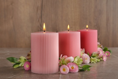 Stylish tender composition with burning candles and flowers on table against wooden background. Cozy interior element