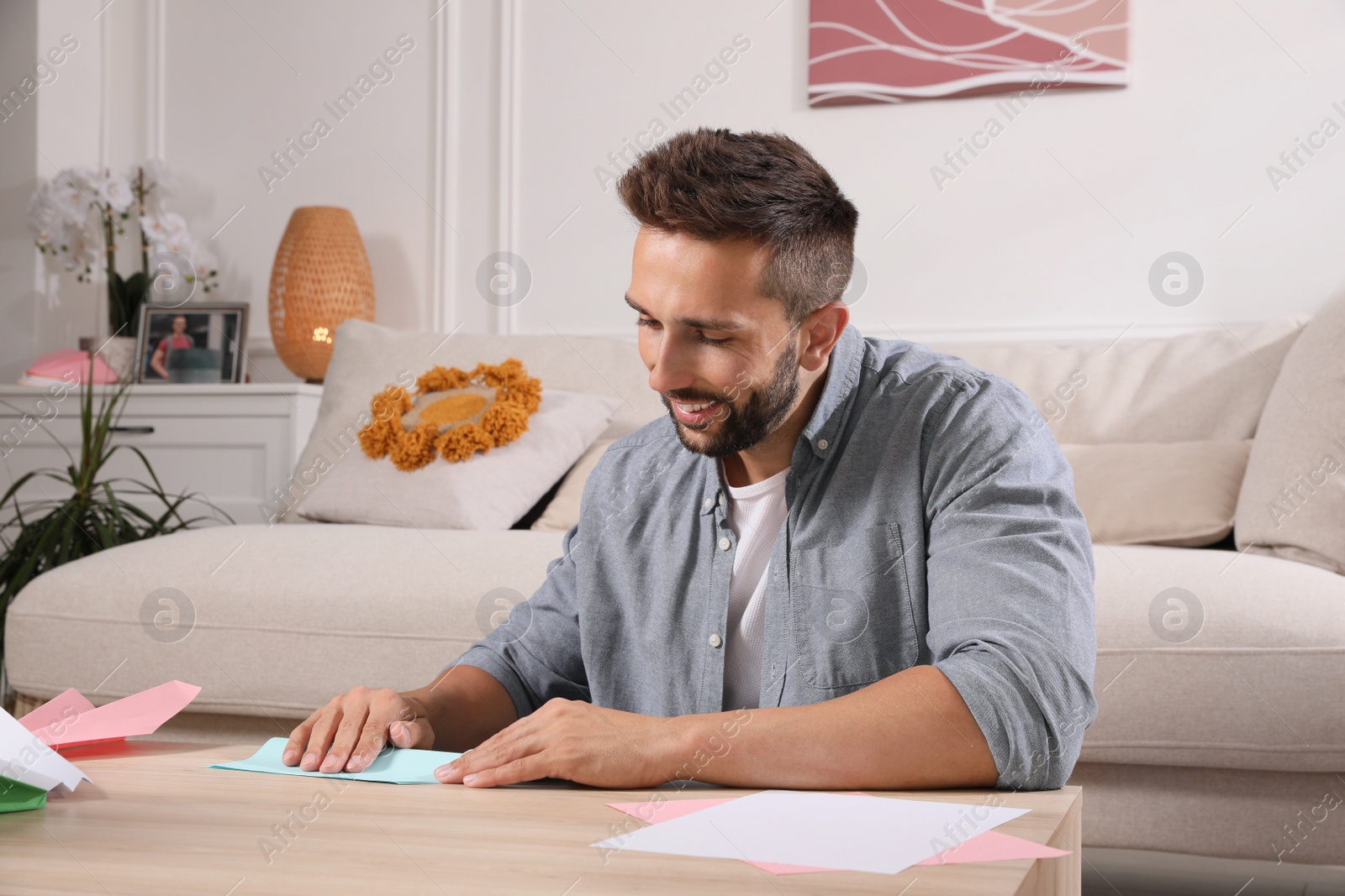 Photo of Happy man making paper plane at desk in living room