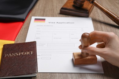 Immigration to Germany. Woman stamping visa application form at wooden table, closeup