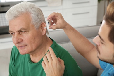 Young man putting hearing aid in father's ear indoors