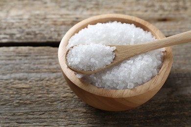 Photo of Organic salt in bowl and spoon on wooden table, closeup. Space for text