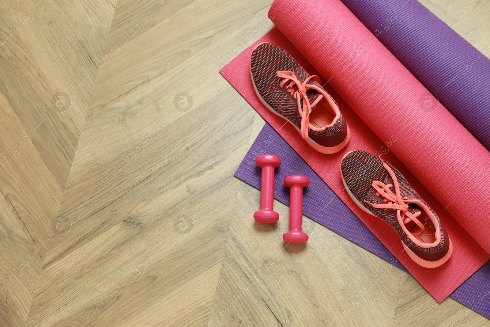 Photo of Dumbbells, sneakers and mats on wooden floor, top view. Space for text