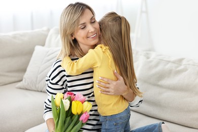 Little daughter congratulating her mom with Mother`s Day at home. Woman holding bouquet of beautiful tulips