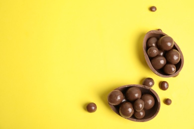 Photo of Halves of tasty chocolate egg with candies on yellow background, flat lay. Space for text