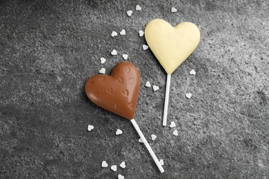 Different chocolate heart shaped lollipops and sprinkles on grey table, flat lay