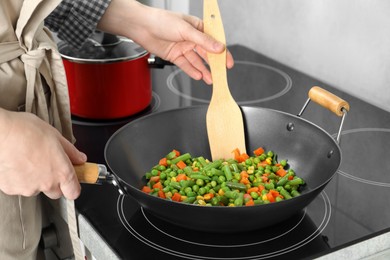 Photo of Woman cooking tasty vegetable mix in wok pan at home, closeup