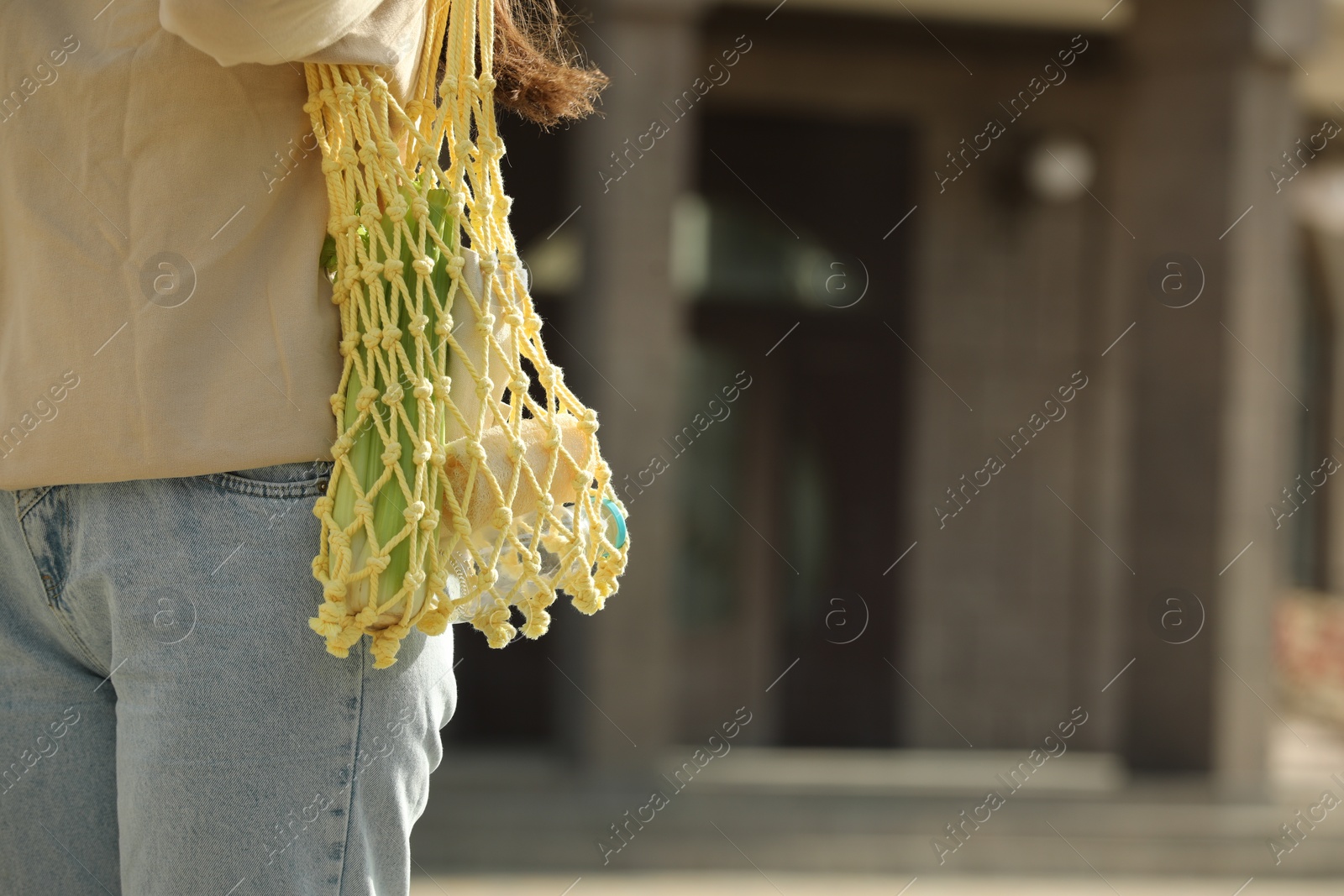 Photo of Conscious consumption. Woman with net bag of eco friendly products outdoors, closeup. Space for text