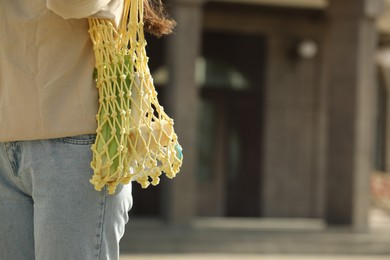 Conscious consumption. Woman with net bag of eco friendly products outdoors, closeup. Space for text
