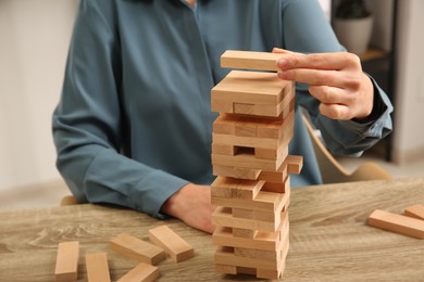 Photo of Playing Jenga. Woman building tower with blocks at wooden table indoors, closeup