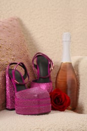 Photo of Pink high heeled shoes with platform, bottle of wine and rose on soft armchair, closeup