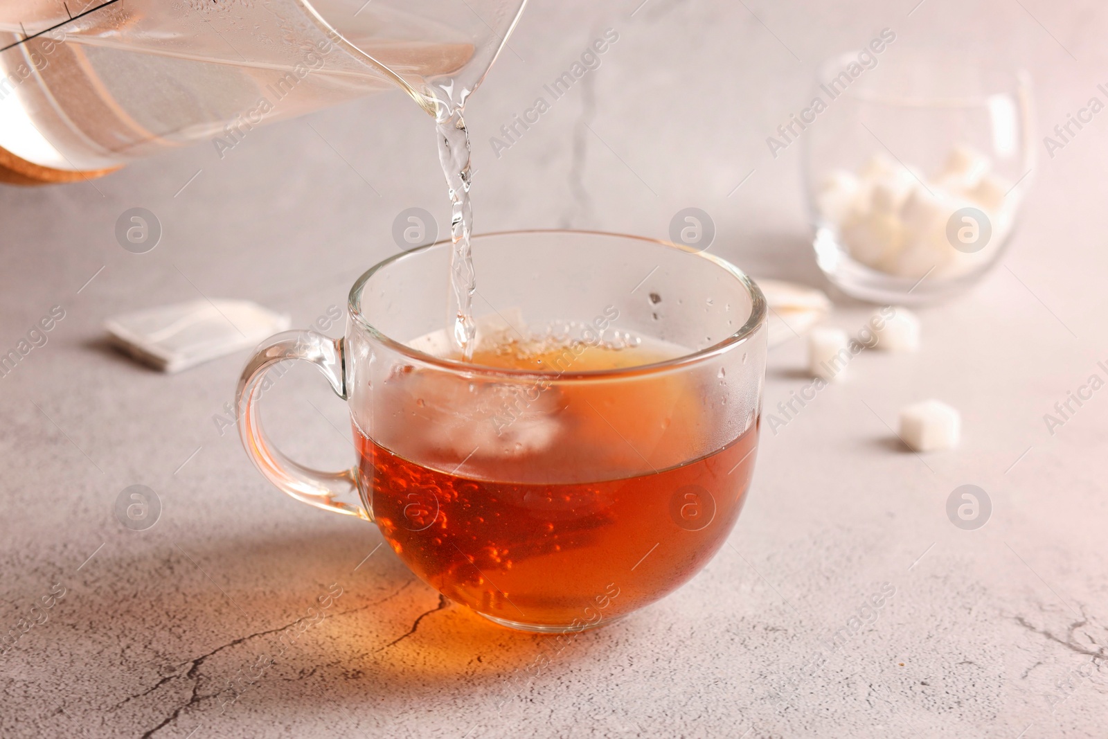 Photo of Pouring hot water into cup with tea bag on light grey textured table, closeup