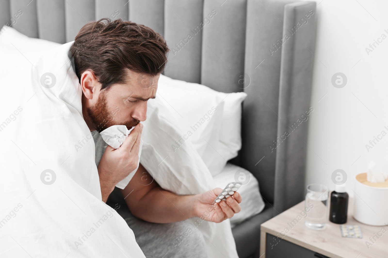 Photo of Sick man with tissue coughing on bed at home. Cold symptoms