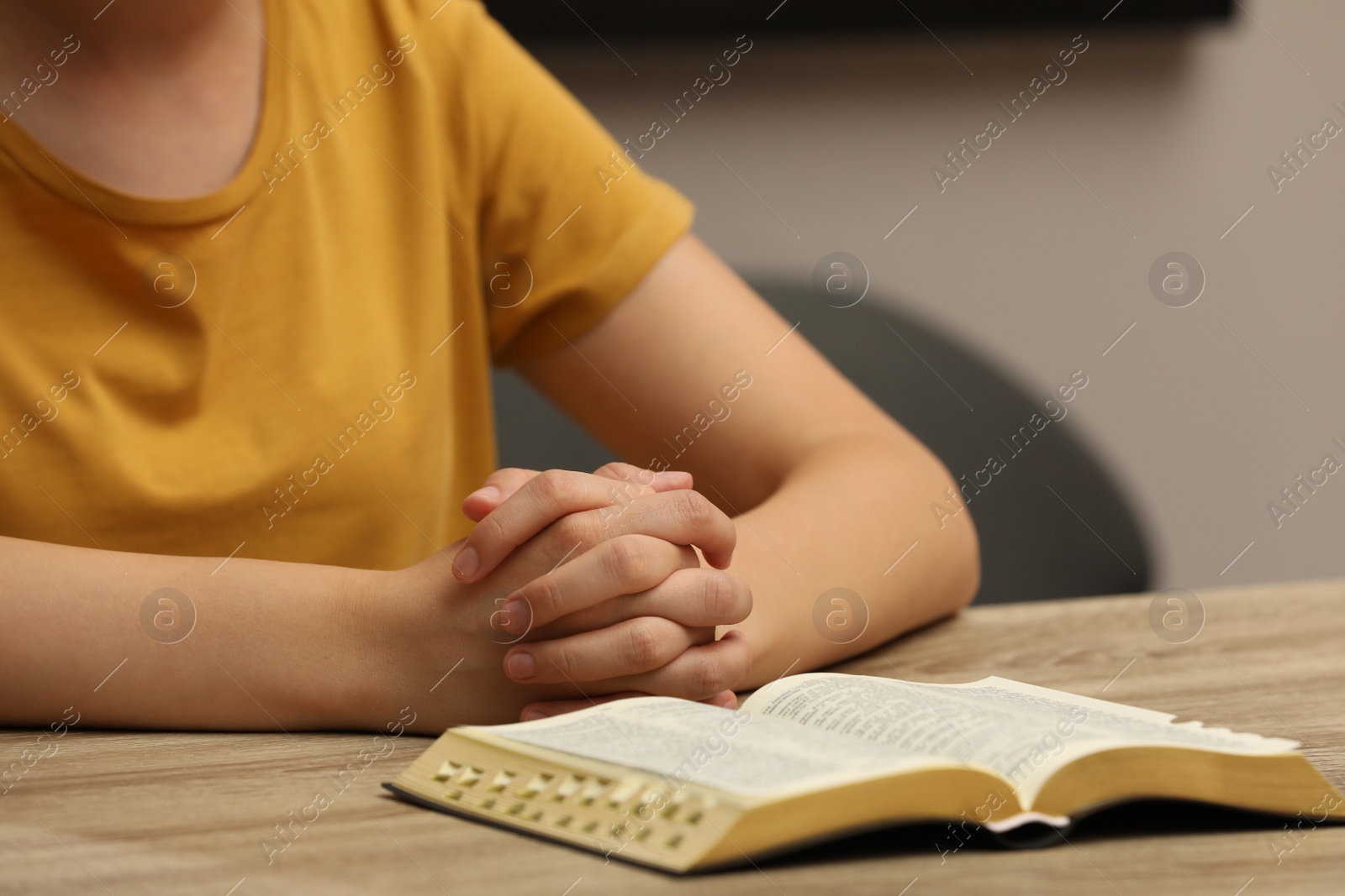 Photo of Religious woman praying over Bible at wooden table indoors, closeup