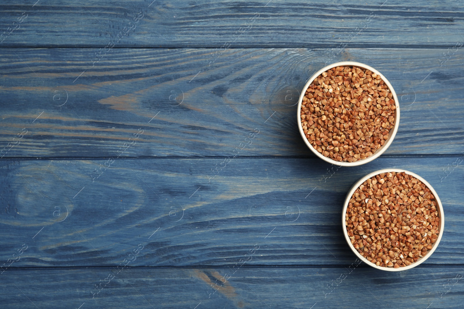 Photo of Buckwheat grains on blue wooden table, flat lay. Space for text