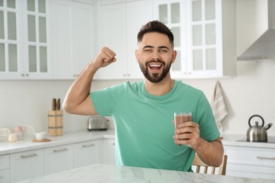 Photo of Young man with glass of chocolate milk showing his strength in kitchen