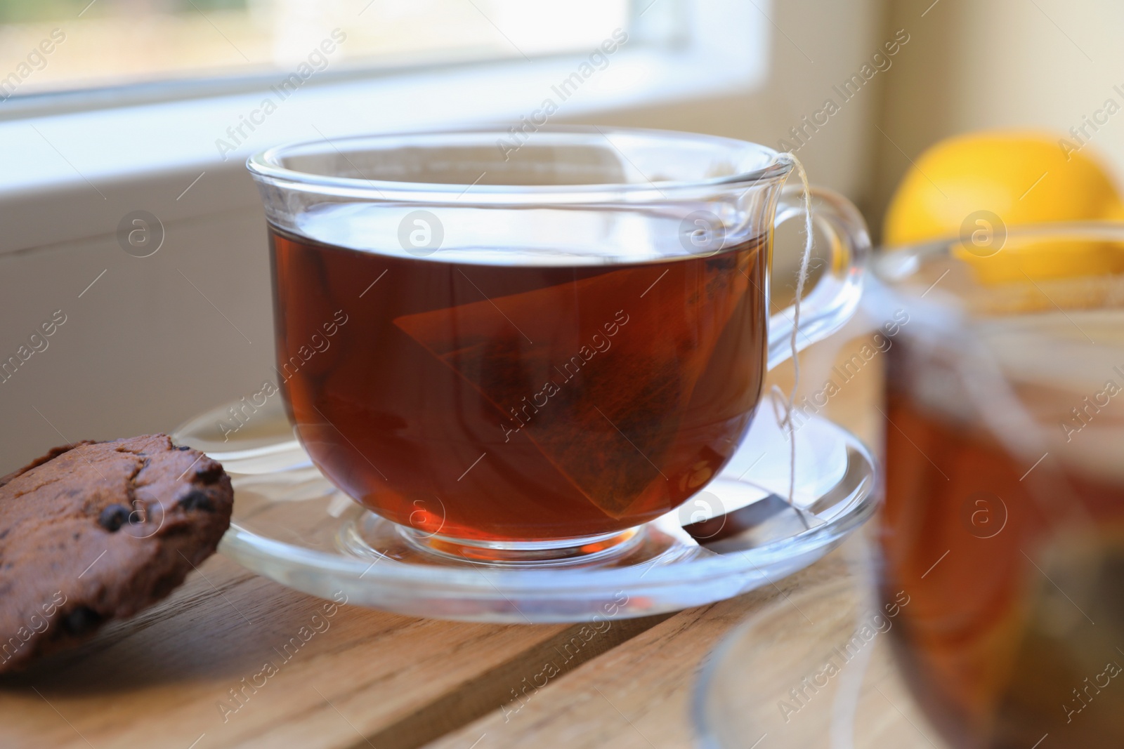 Photo of Bag of black tea in cups on wooden table indoors, closeup