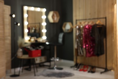 Photo of Blurred view of makeup room with stylish mirror near dressing table, chair and clothes rack