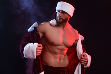 Attractive young man with muscular body in Santa costume on black background