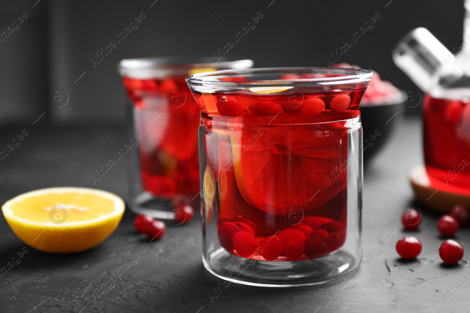 Photo of Tasty hot cranberry tea with lemon and fresh berries in glass on black textured table