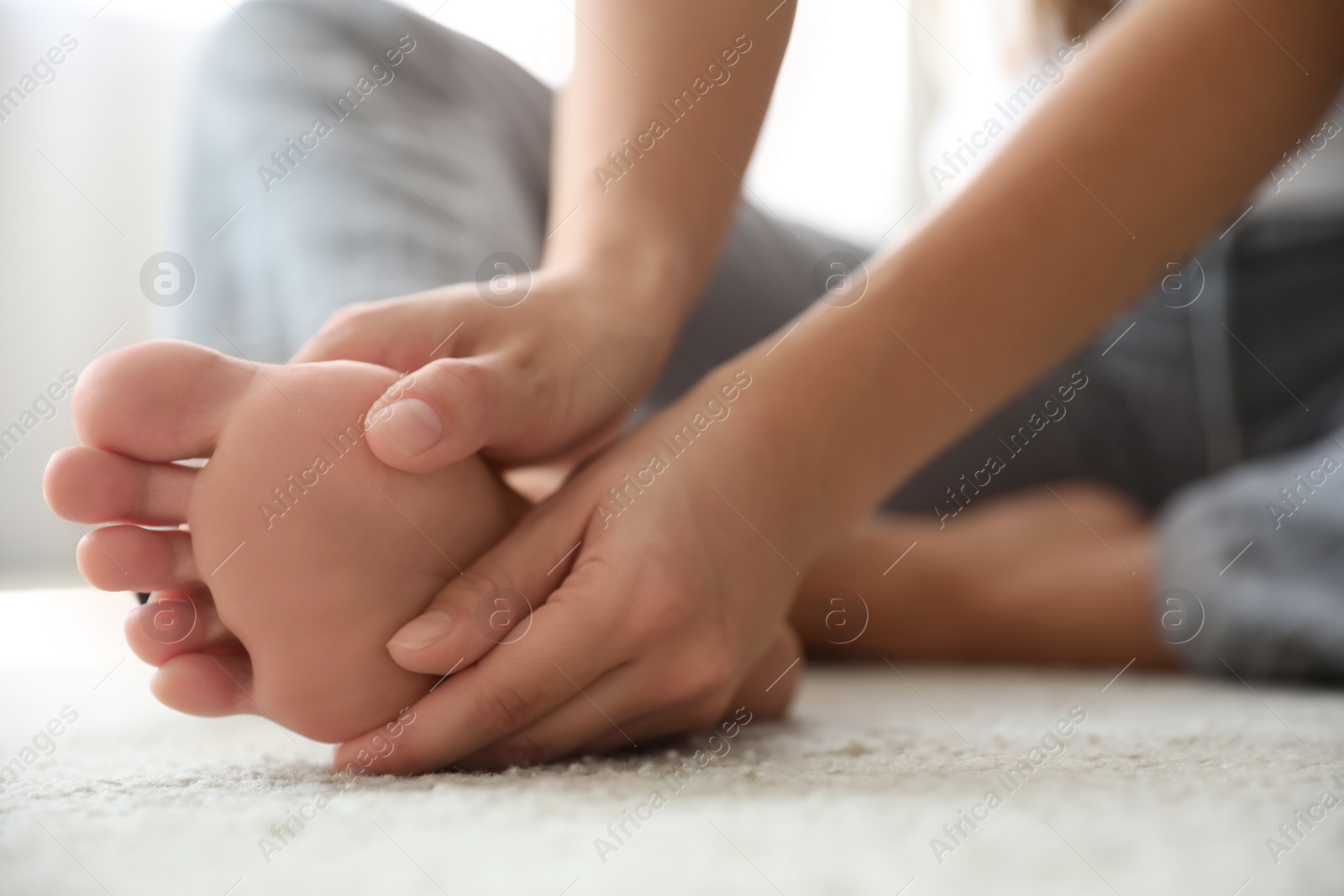 Photo of Young woman suffering from pain in foot on floor, closeup