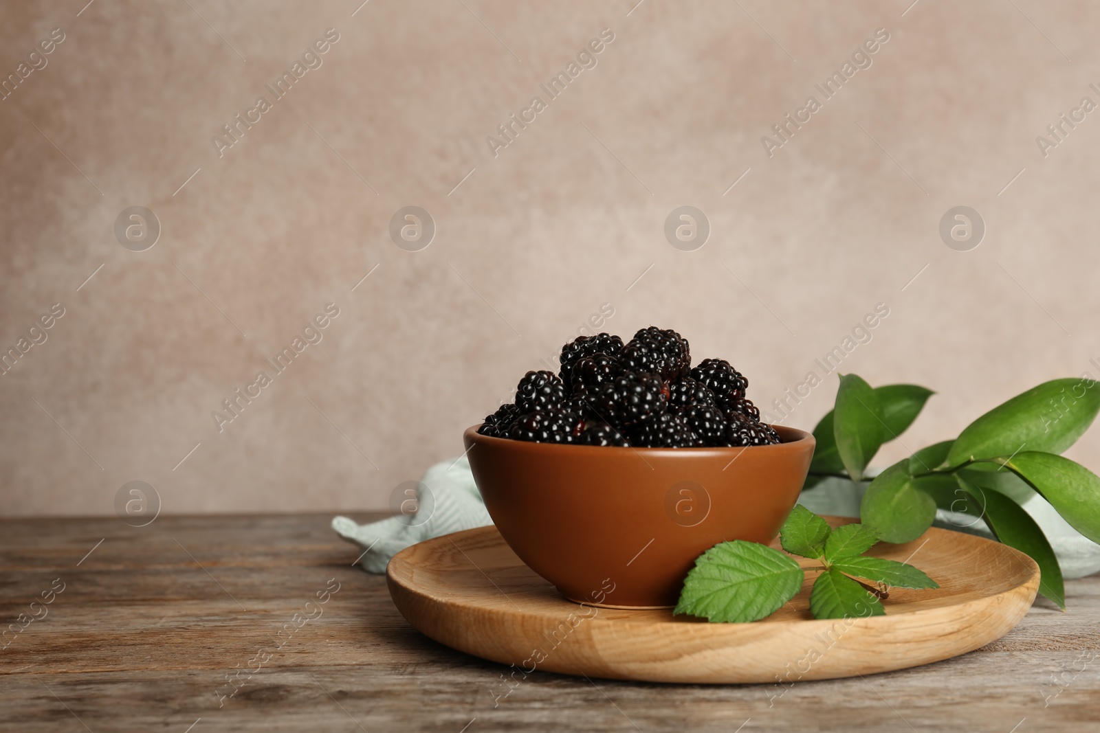 Photo of Bowl with fresh blackberry on wooden table against color background