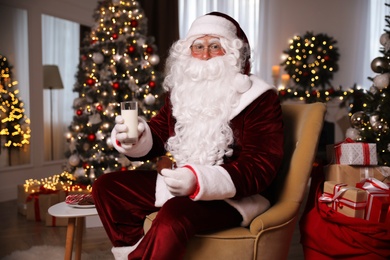 Photo of Santa Claus with glass of milk and cookie in room decorated for Christmas