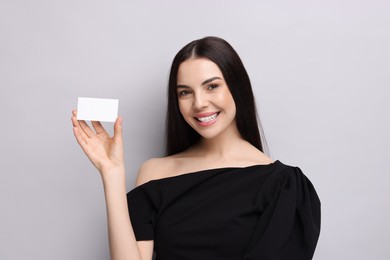 Happy woman holding blank business card on light grey background