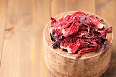 Photo of Dry hibiscus tea in bowl on wooden table, closeup