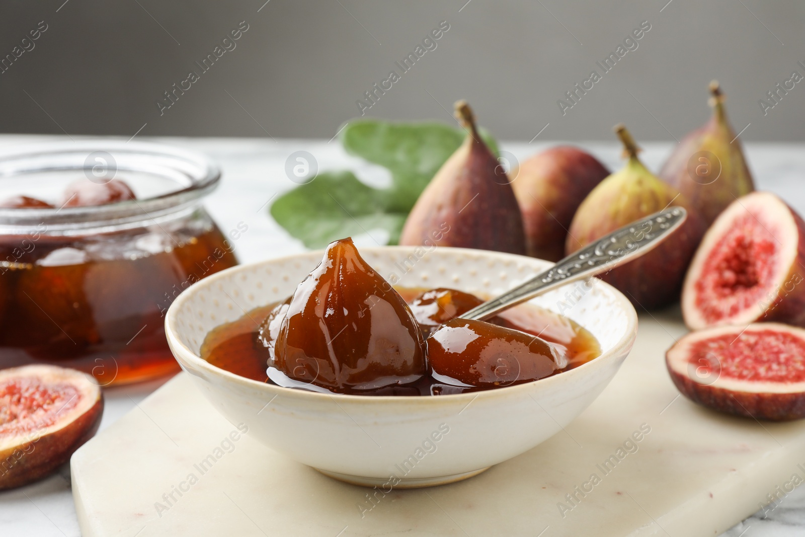 Photo of Bowl of tasty sweet jam and fresh figs on white marble table