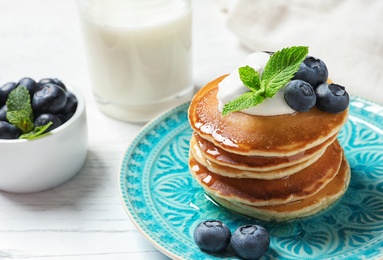 Photo of Plate of tasty pancakes with blueberries, sauce and mint on white wooden table, closeup