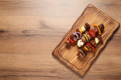 Photo of Delicious shish kebabs with vegetables on wooden table, top view. Space for text