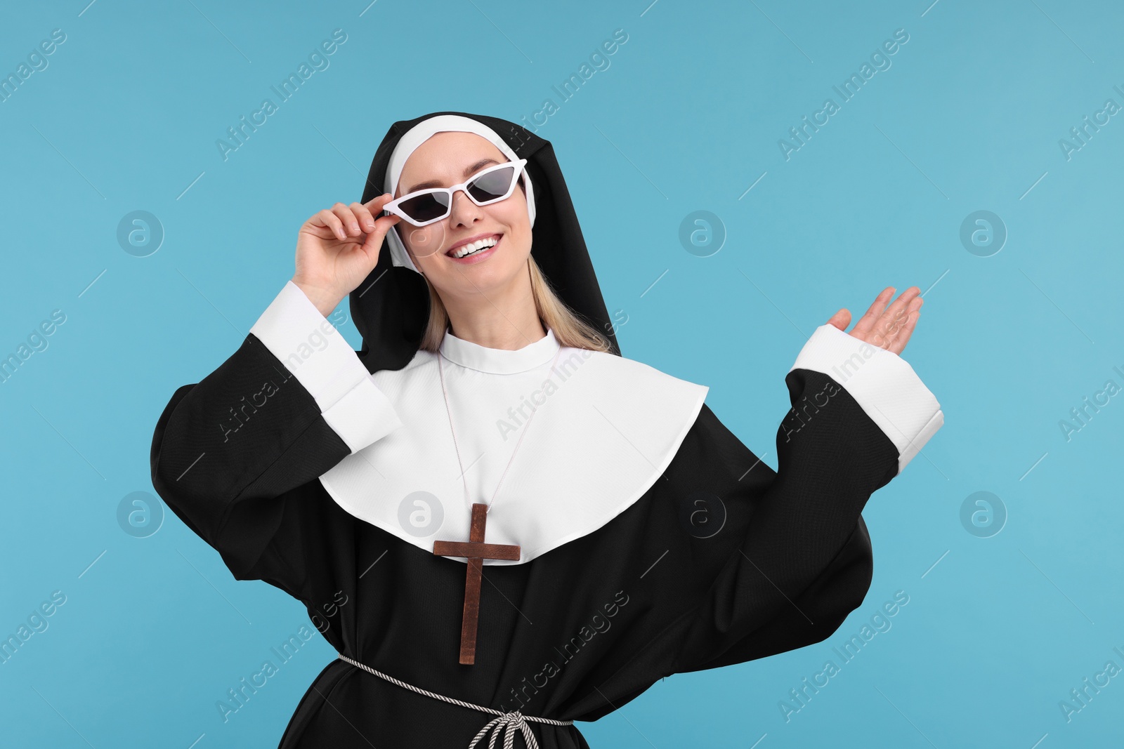 Photo of Happy woman in nun habit and sunglasses against light blue background