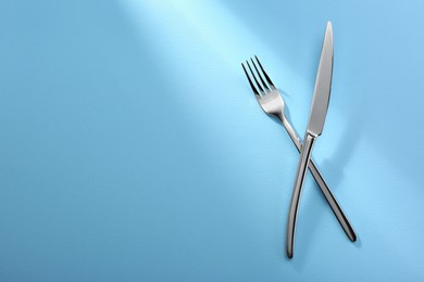 Shiny fork and knife on light blue background, flat lay. Space for text