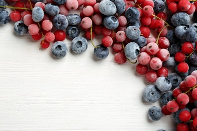 Tasty frozen blueberries and red currants on white wooden table, flat lay. Space for text