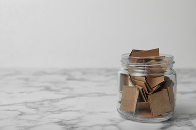 Glass jar with paper pieces on white marble table, space for text