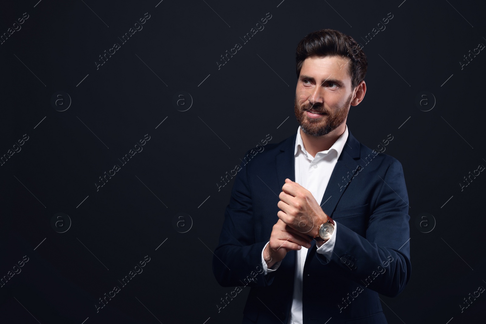 Photo of Handsome bearded man adjusting cufflinks on black background. Space for text