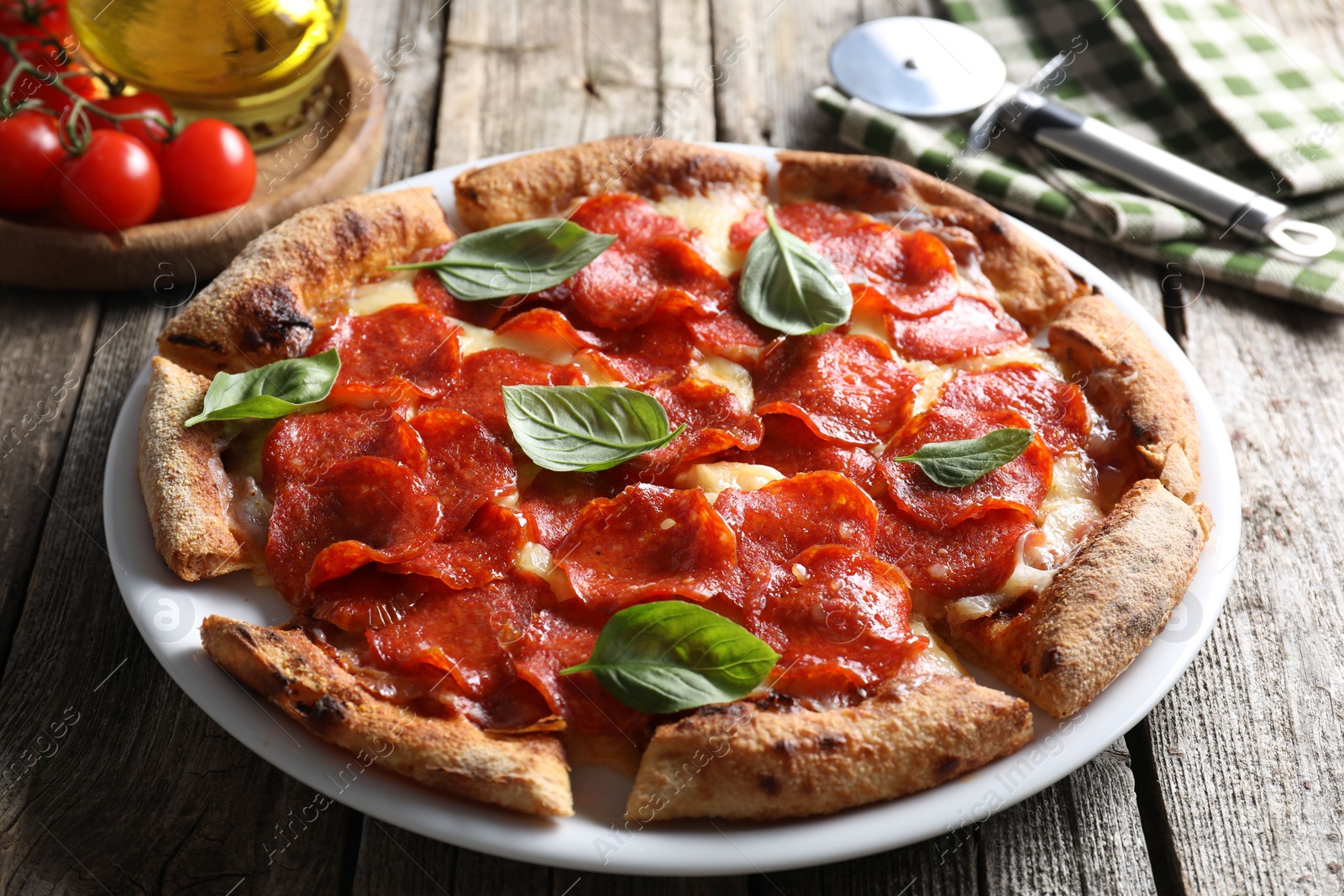 Photo of Tasty pepperoni pizza with basil, tomatoes and cutter on wooden table