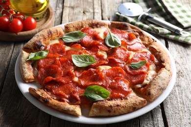 Tasty pepperoni pizza with basil, tomatoes and cutter on wooden table