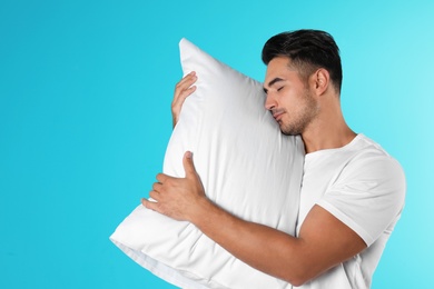 Young man with soft pillow on color background