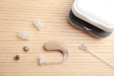 Hearing aid and accessories on wooden background, flat lay