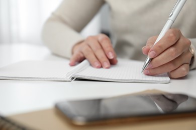 Photo of Left-handed woman writing in notebook at table indoors, closeup