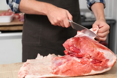 Butcher cutting fresh raw meat on counter in shop, closeup