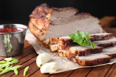 Photo of Pieces of baked pork belly served with sauce and parsley on wooden board, closeup