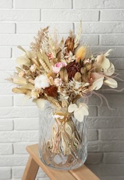 Photo of Beautiful dried flower bouquet in glass vase on wooden ladder near white brick wall