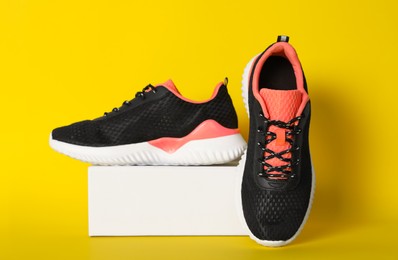 Photo of Pair of stylish sport shoes and box on yellow background