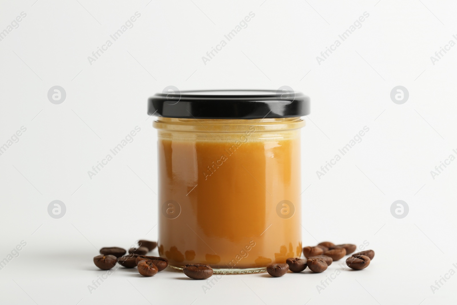 Photo of Tasty salted caramel in jar and coffee beans on white background