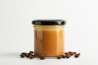 Tasty salted caramel in jar and coffee beans on white background