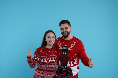 Photo of Happy young couple in Christmas sweaters showing thumbs up on light blue background